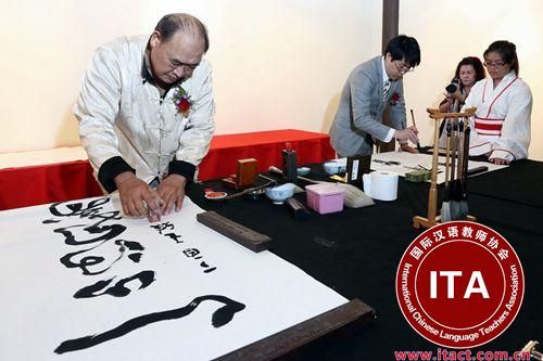 中国侨网马来西亚书艺协会会长王雅（左）在完成作品后盖上姓名印章，于乐（右）专注挥毫。（马来西亚《星洲日报》）